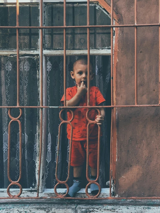 the little boy is standing behind an orange fence