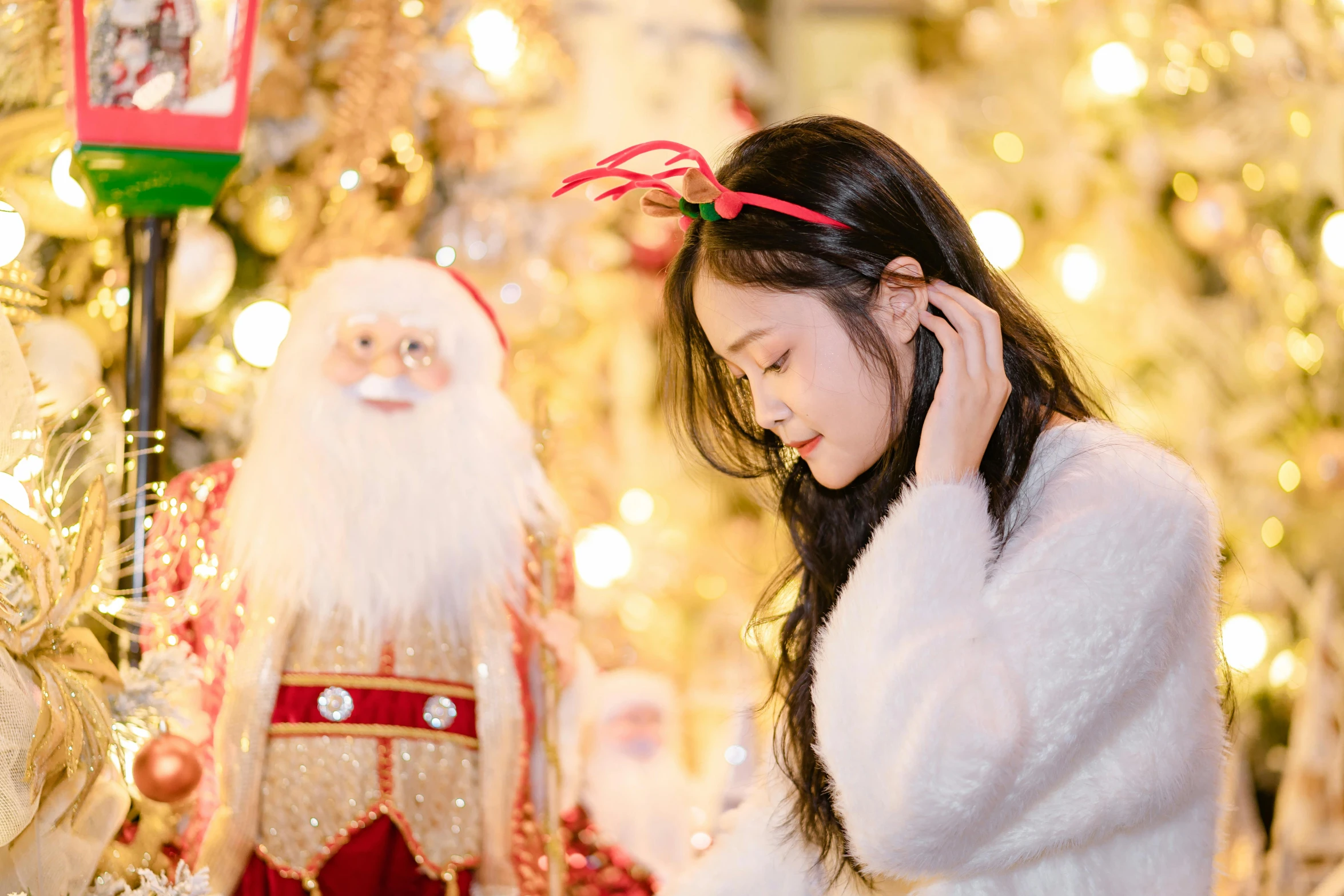 an oriental girl in a santa clause outfit talks on her cell phone next to the christmas tree