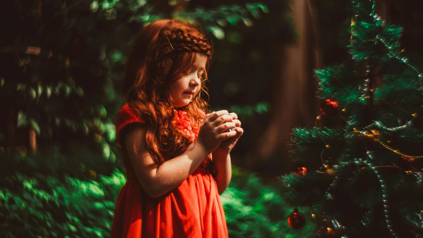 a  in an orange dress stands near a small christmas tree