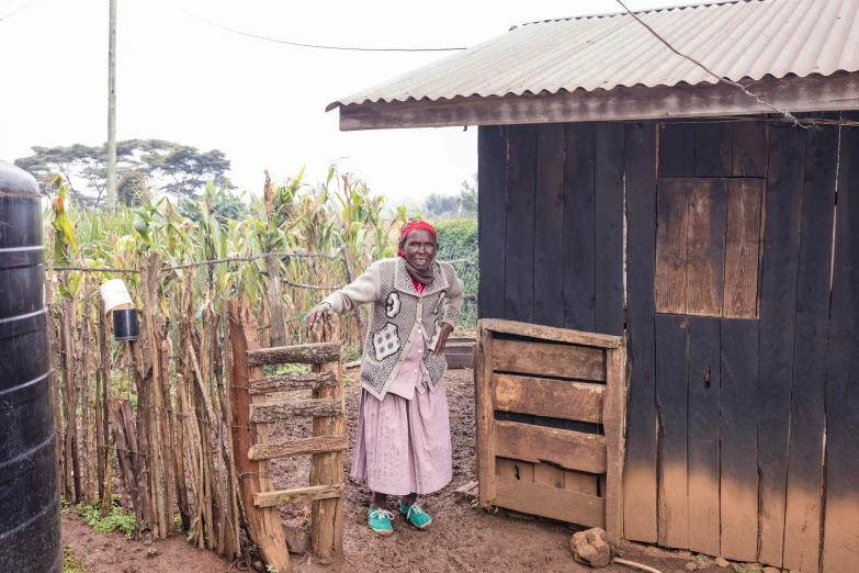 a woman stands outside a shack that contains crops