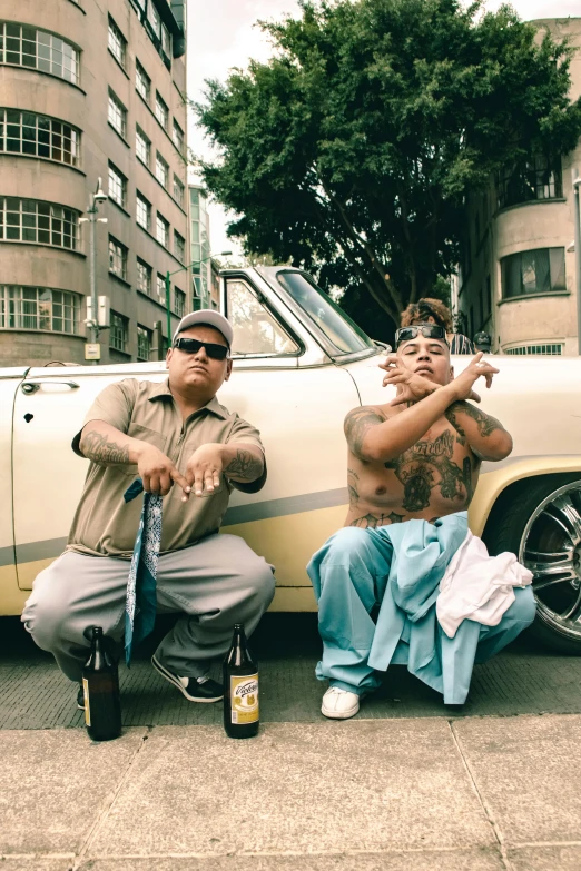 two men are sitting and posing near a car