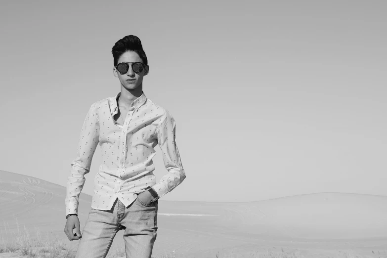 a man wearing sunglasses standing in a dry grassy field