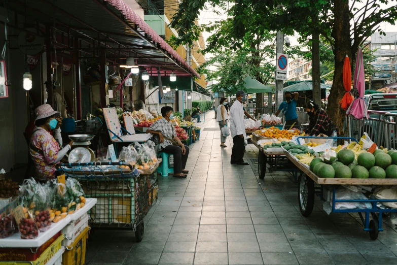 people on a sidewalk with carts full of fruits