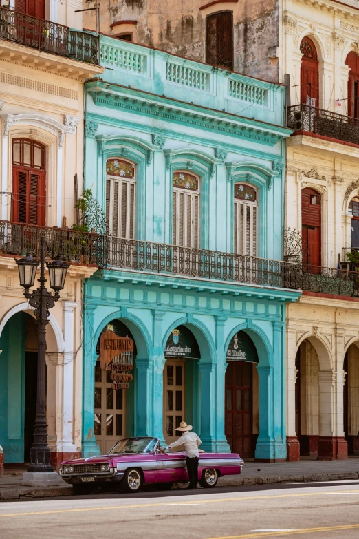 an old pink and blue building with two cars parked in front