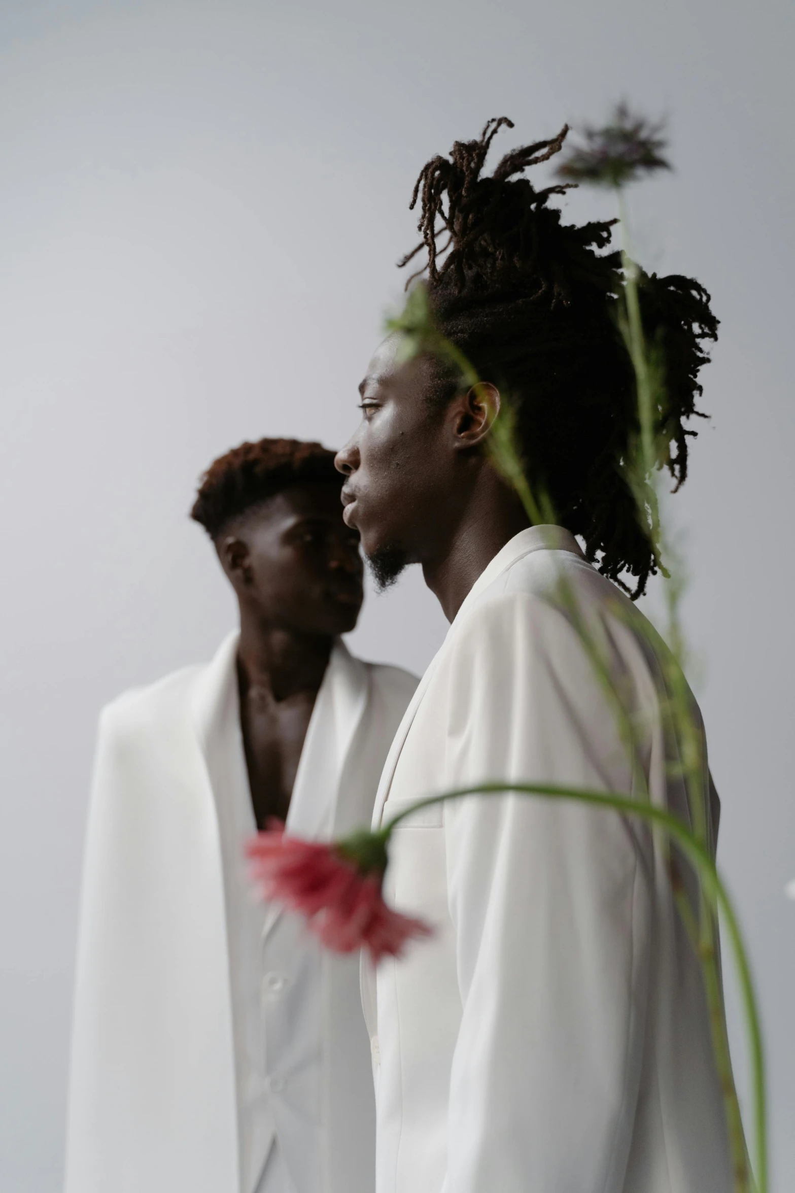 two young men stand next to each other near a flower