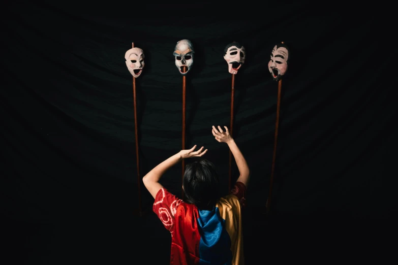 a person holding several masks behind them against a black background