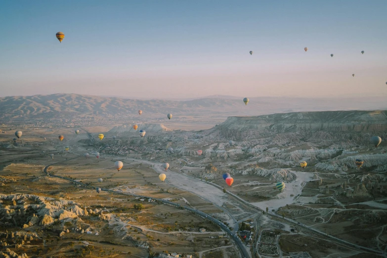 several balloons fly over a valley and mountains