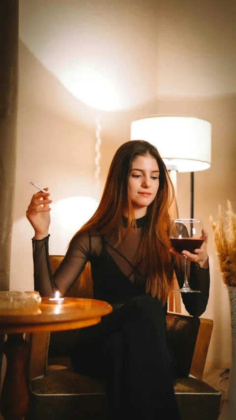 a beautiful young woman in a black top sitting at a table with a wine glass