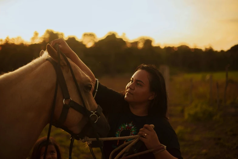 a girl and her horse are outside while the sun is set