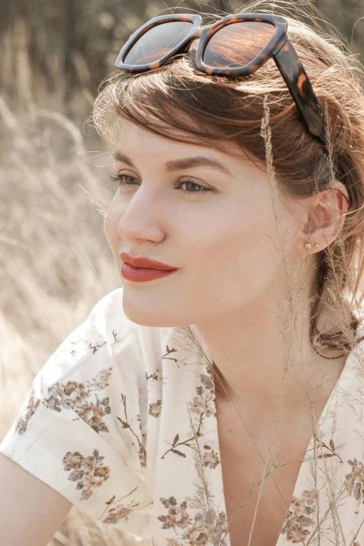 a beautiful woman sitting in a field wearing shades