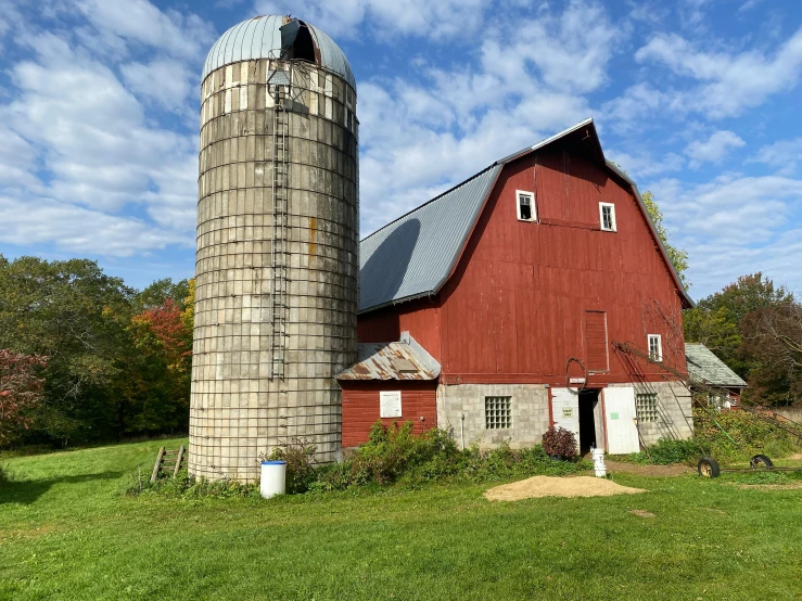 a barn sitting on top of a green field next to a tall silo