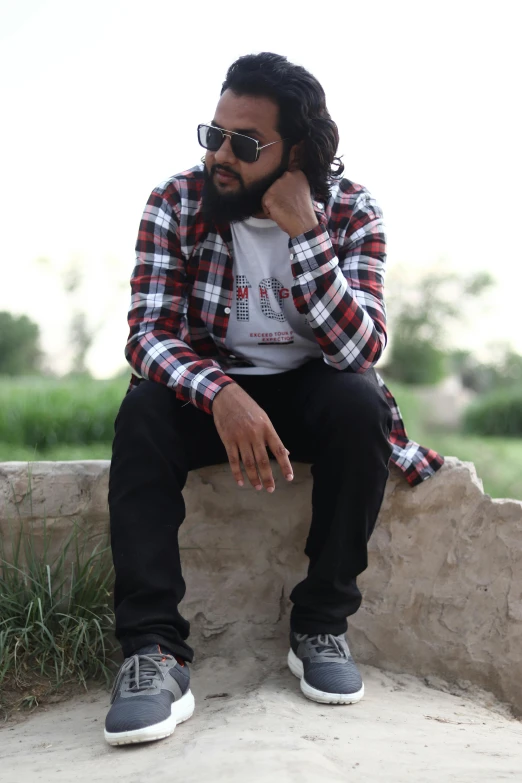 man sitting on stone bench wearing plaid shirt and sunglasses