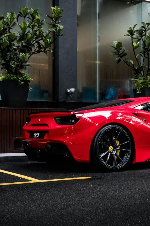 the back end of a red car parked in front of a tall building