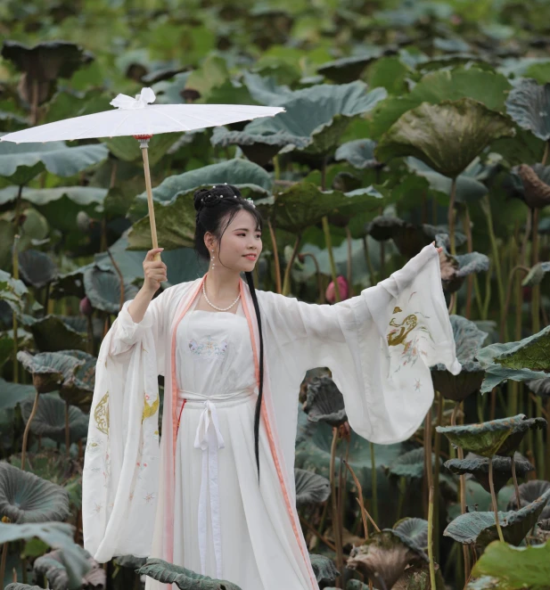 a woman wearing white and holding an umbrella in front of green plants
