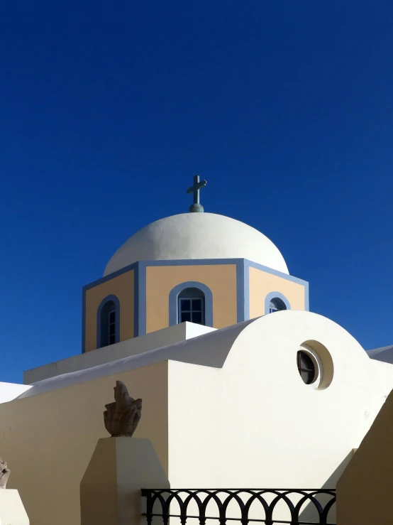 the white building is behind a cross and some bushes