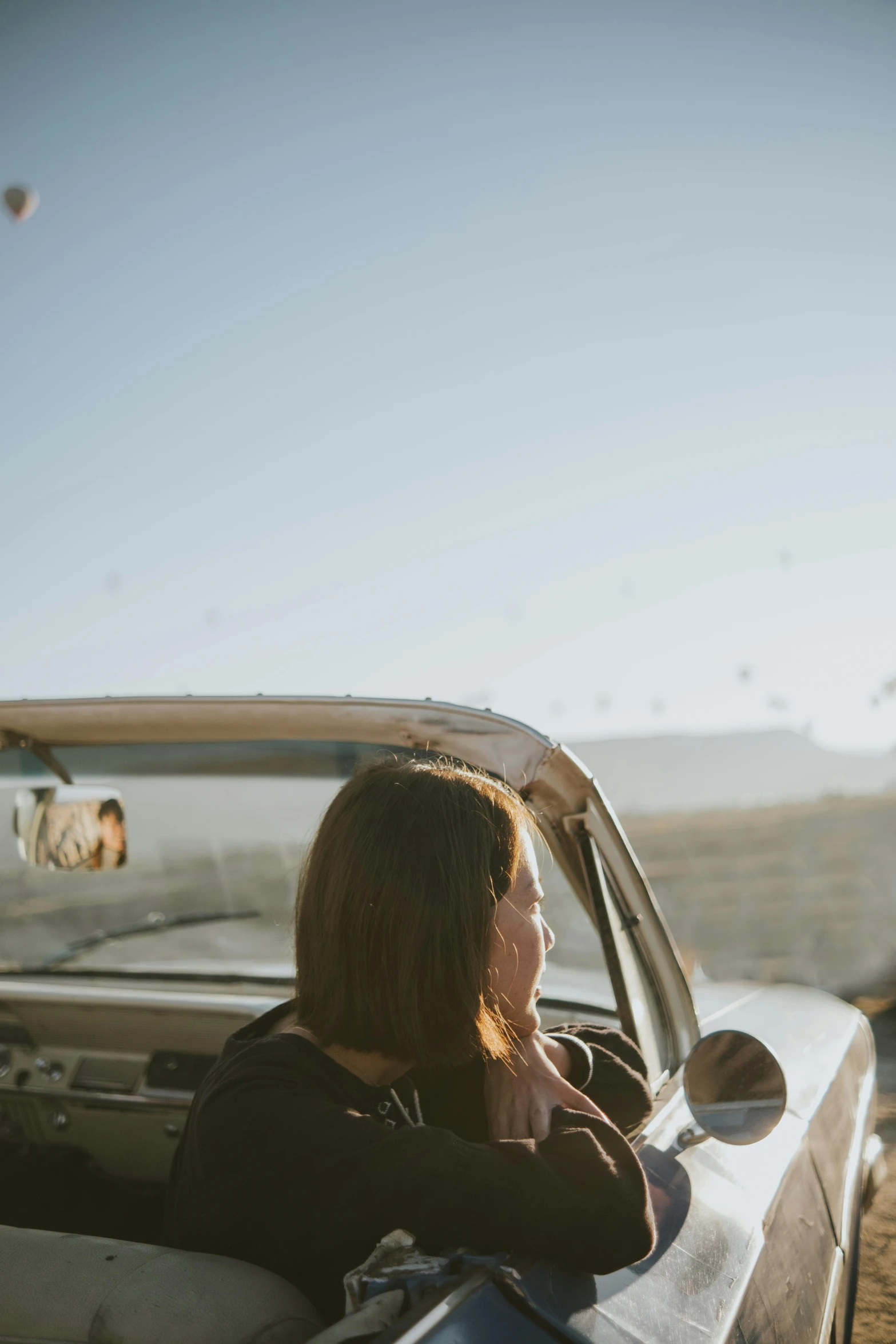 a young woman looks out the car window, near a  air balloon