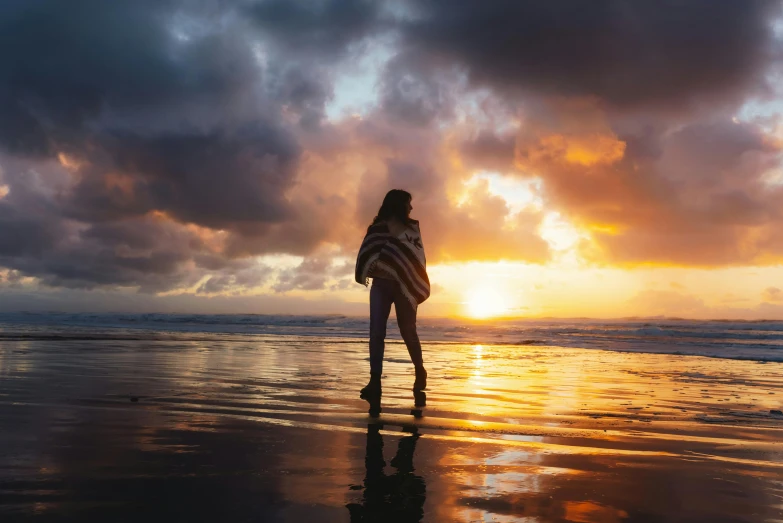 a woman walking along the beach at sunset