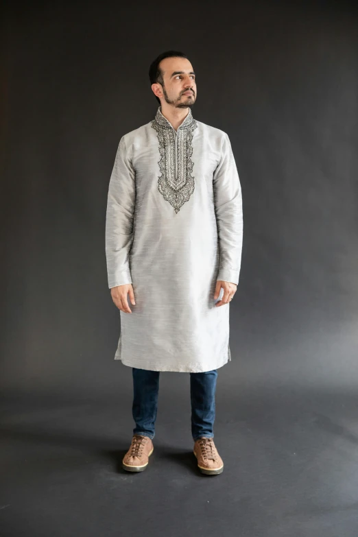 a man in a light gray tunic standing and smiling