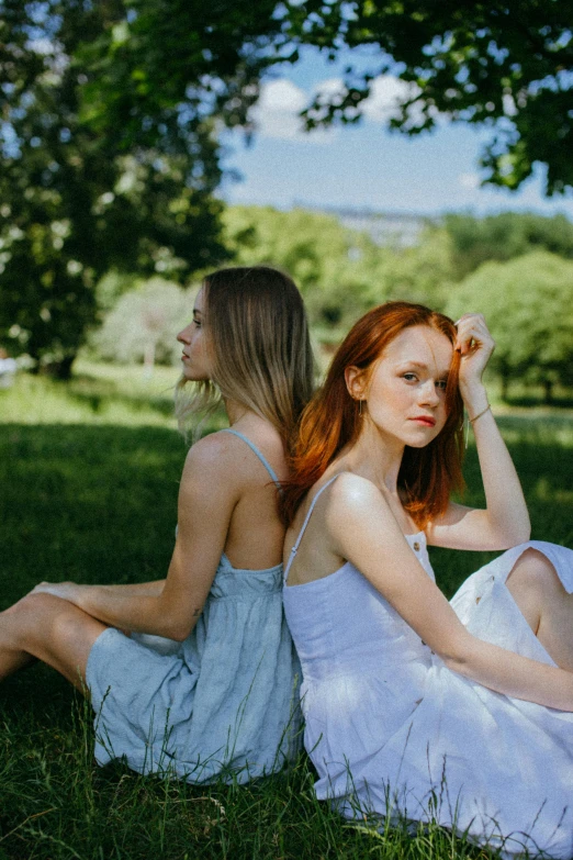 two women sitting in the grass holding their hair