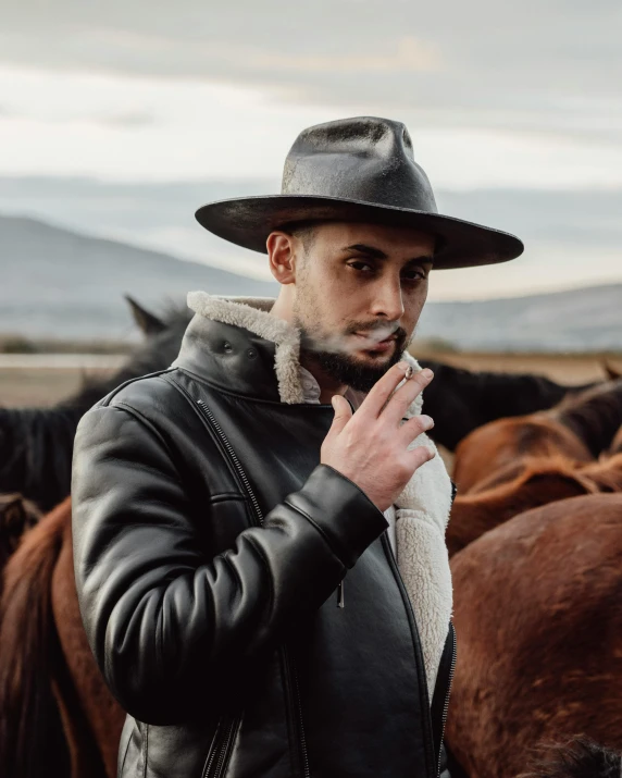 man wearing a hat standing in a field with horses