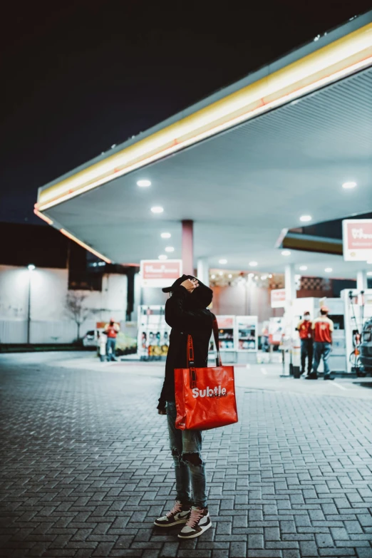 woman standing outside of gas station with bag