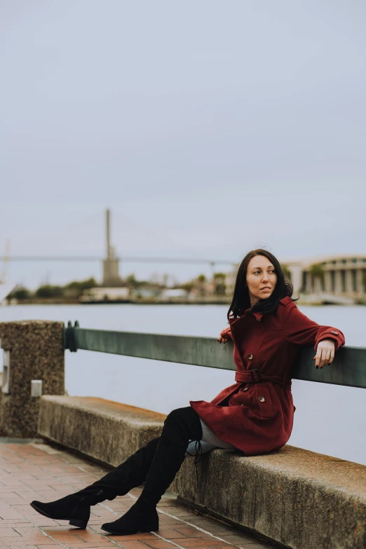 a woman in red is sitting on a stone curb by the water