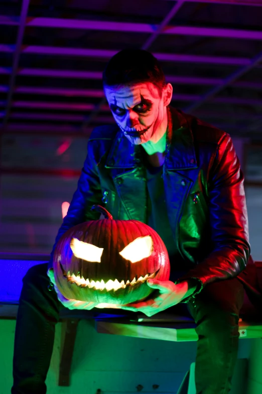 a guy is sitting in a room holding a pumpkin