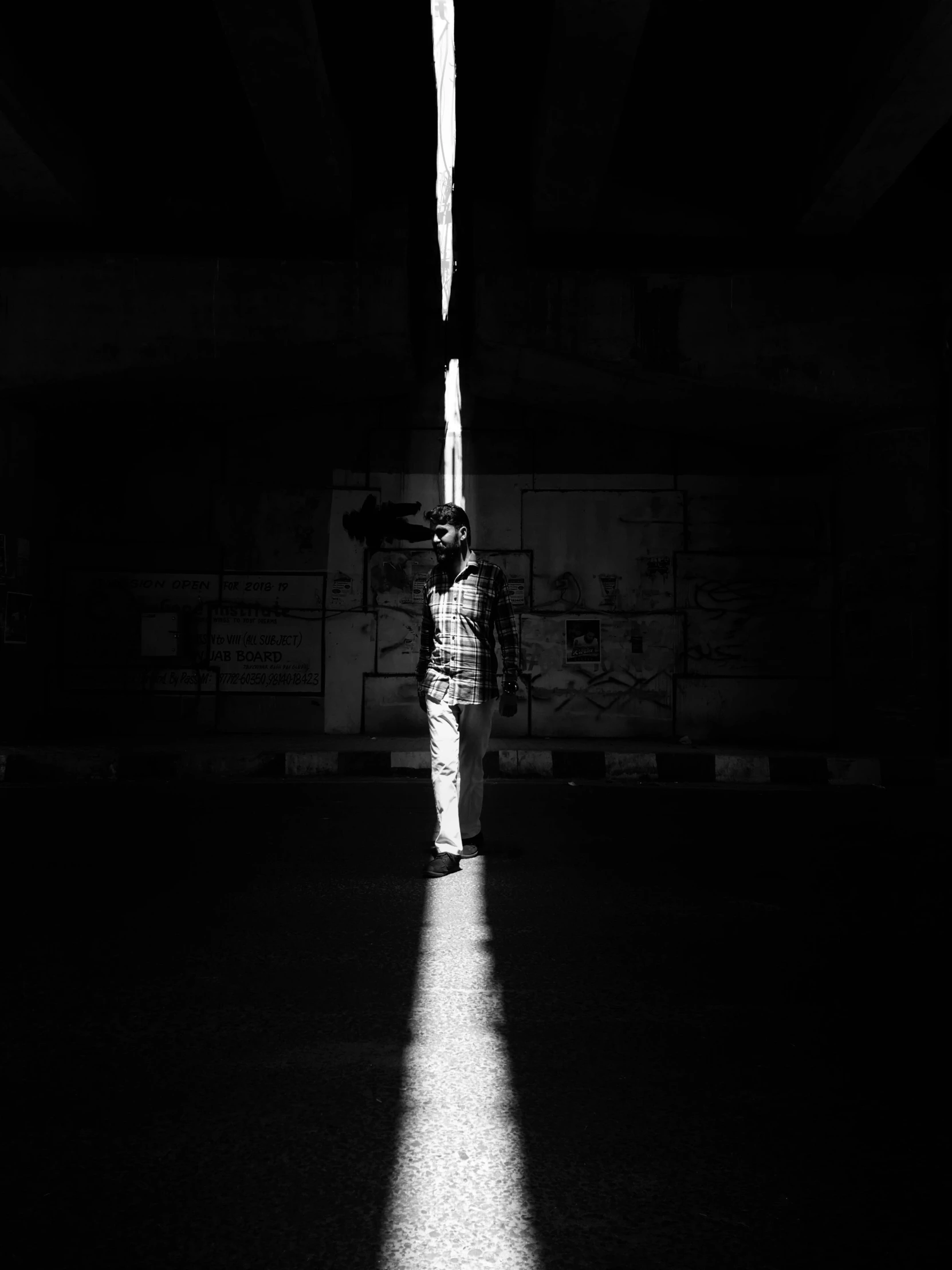 man with umbrella standing next to street sign in black and white po