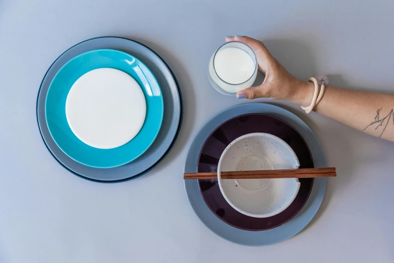 a person holds a glass with chopsticks next to some white plates