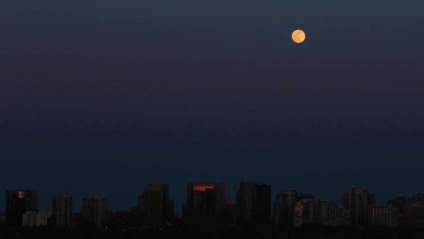 the full moon shining bright above some tall buildings