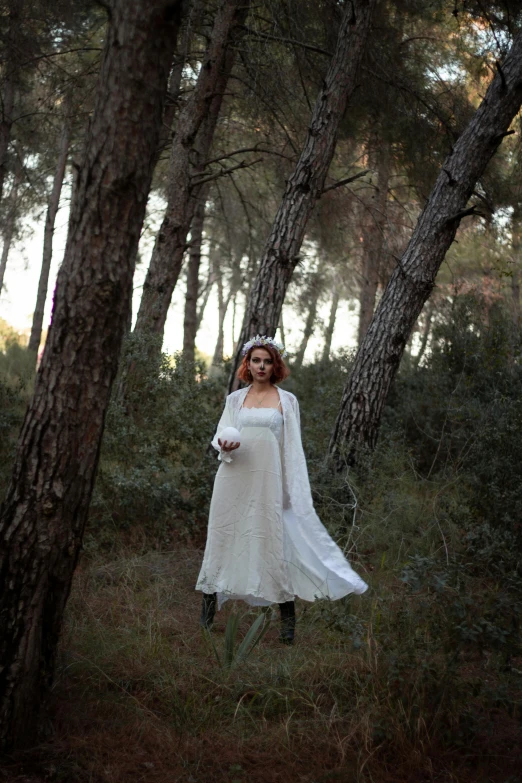 a young lady in a long white dress stands in the forest