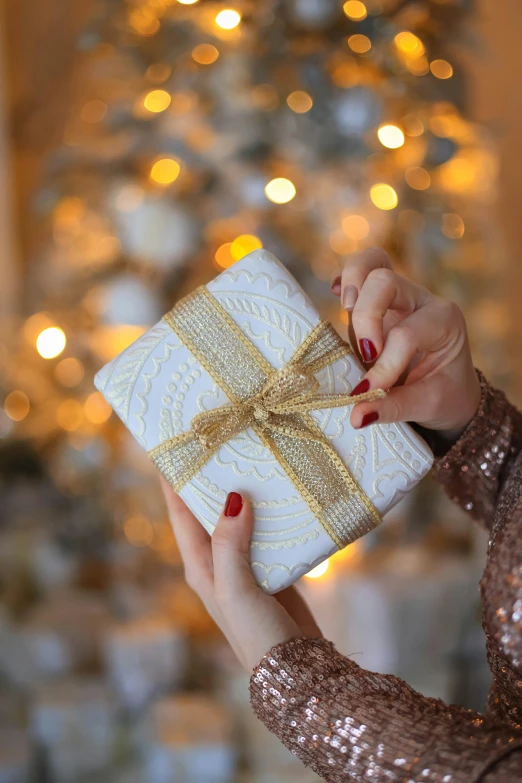 a woman holding onto a wrapped present in front of a decorated tree