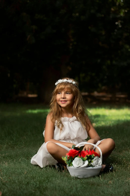 the little girl is sitting in the grass with a basket