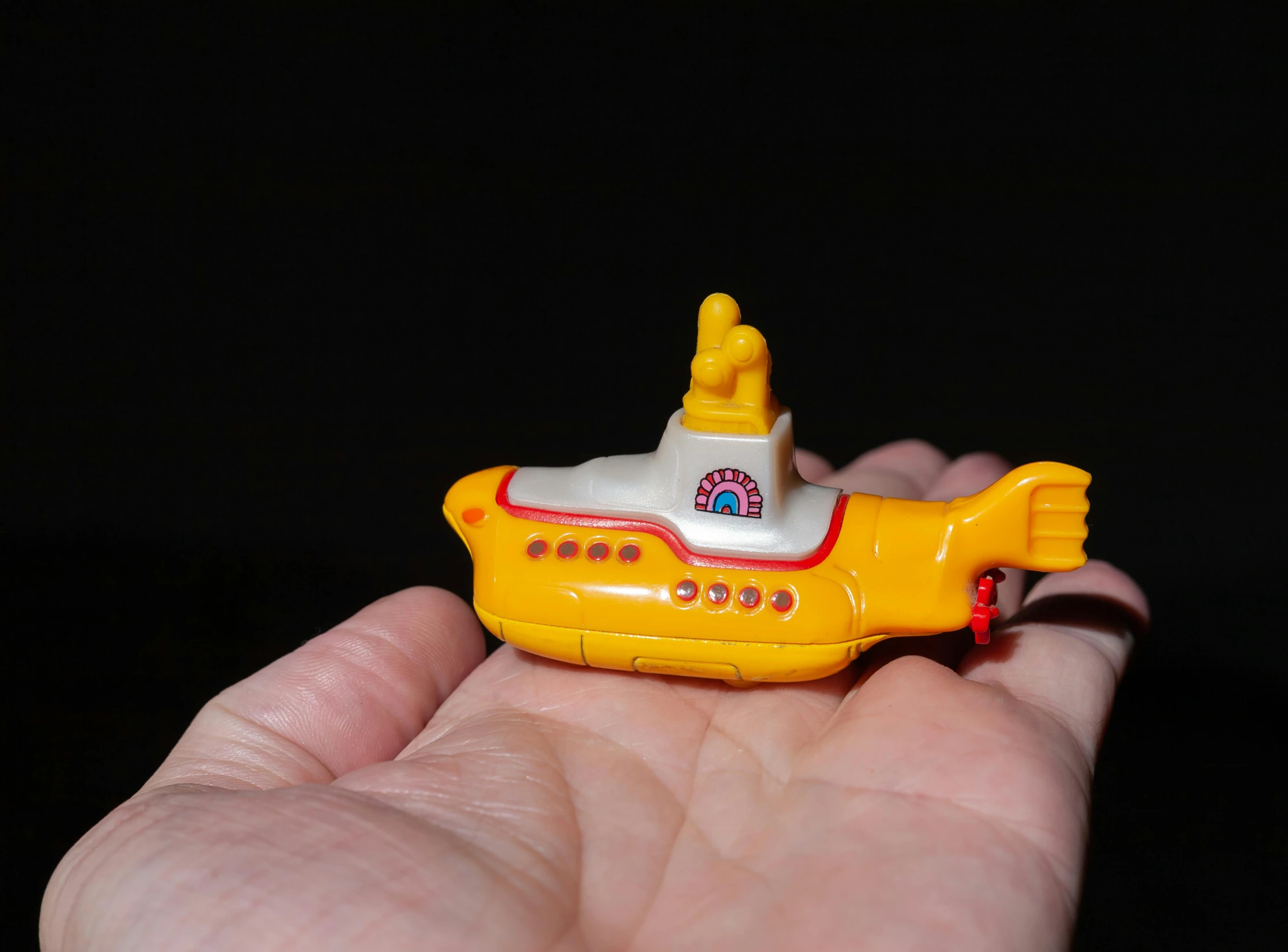 a hand holding a small toy yellow submarine in the dark