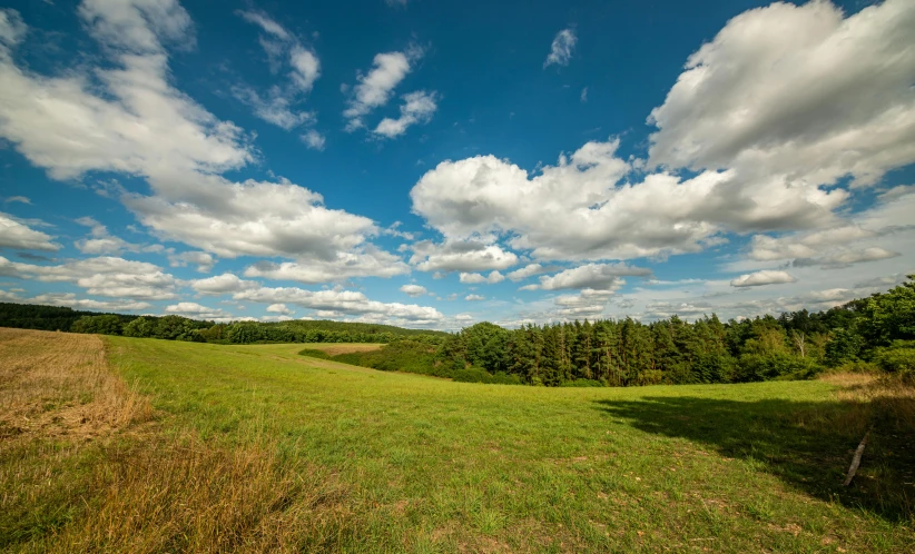 a wide open field covered with grass and clouds