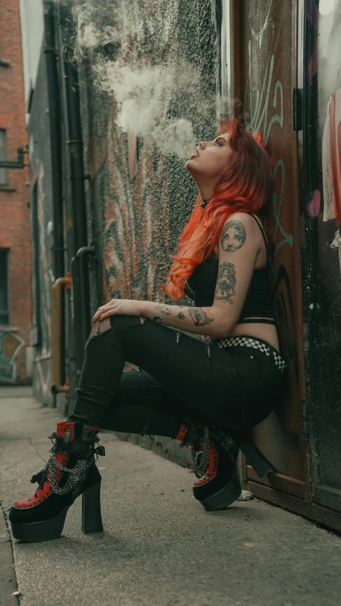 a lady with red hair sitting next to a building and smoking a cigarette