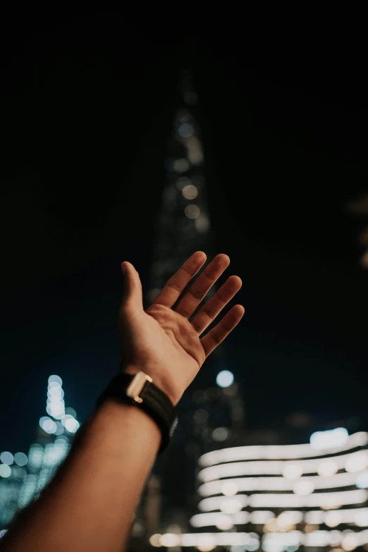 someones hand outstretched in front of the city at night