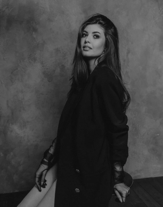 a woman in a black coat with her legs up and a black handbag is sitting on the back of a chair