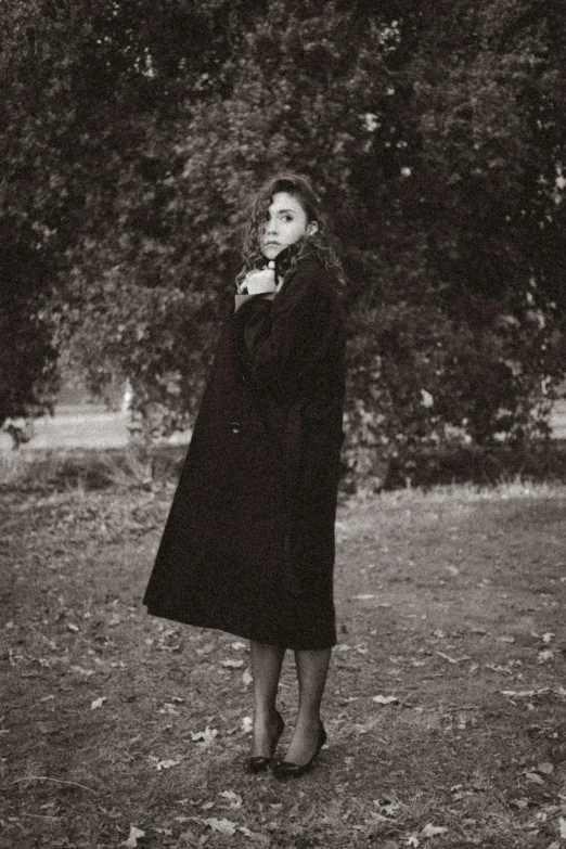 a woman in black coat and gloves walking through the park