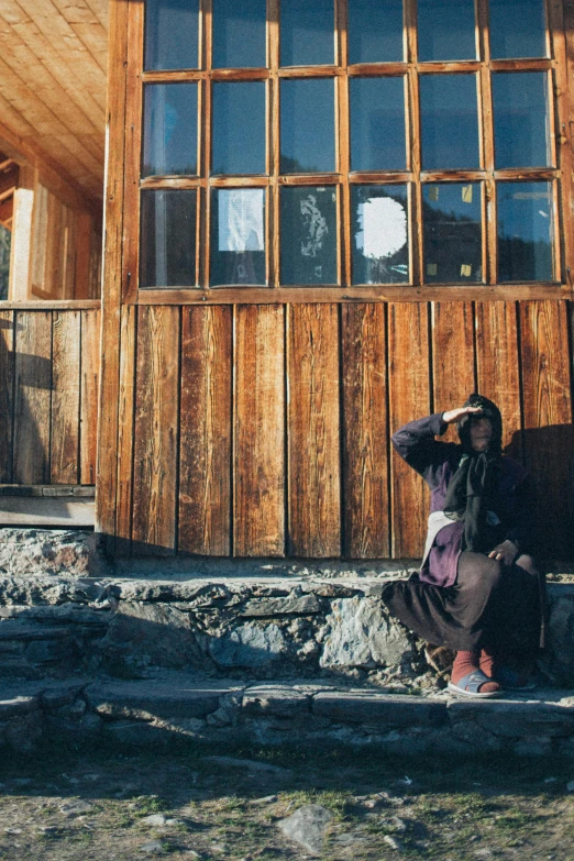 the lady sits in front of the wooden house