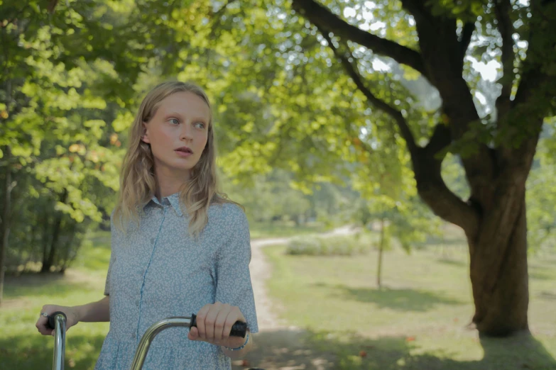 a woman standing in the middle of a park holding a bike