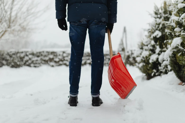 man holding red broom in snowy yard area