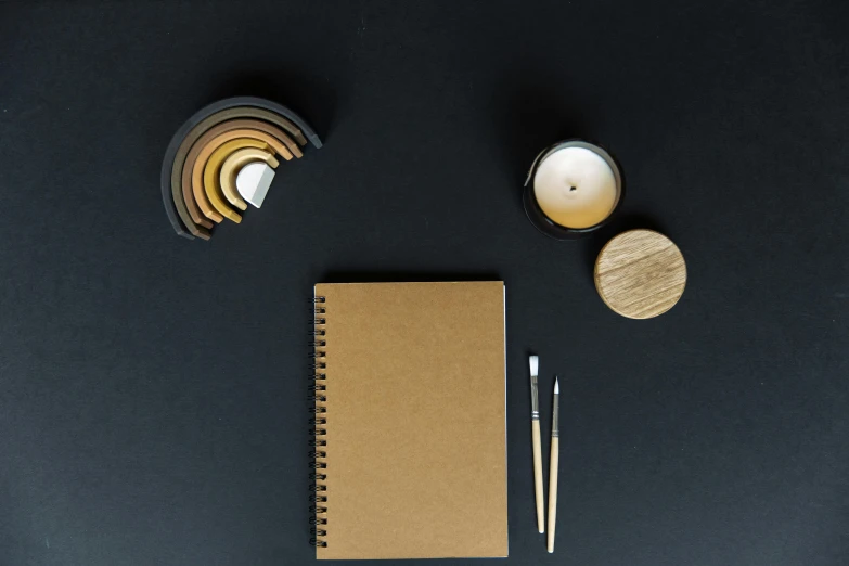 a notebook with pens, candle and other things on a black table