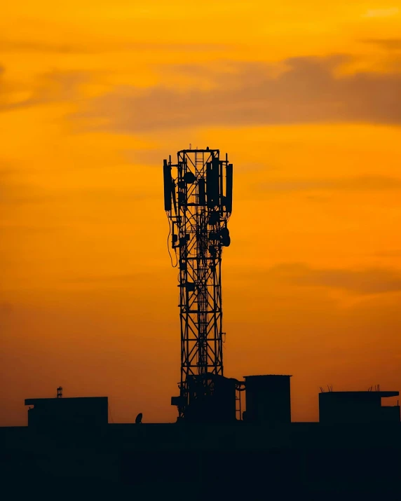 a cell phone tower in silhouette against an orange sunset