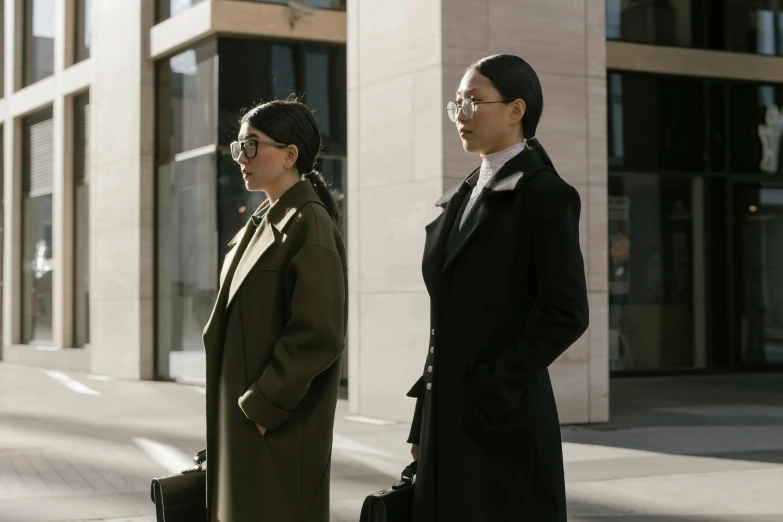 two ladies wearing black, one of them is standing out side with bags