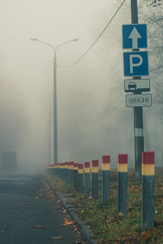 the road sign in fog is next to many yellow and red cones