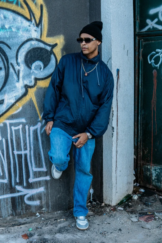 a man wearing jeans and sunglasses leaning against a building