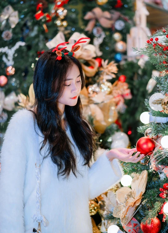 a woman standing near a christmas tree looking at a cellphone