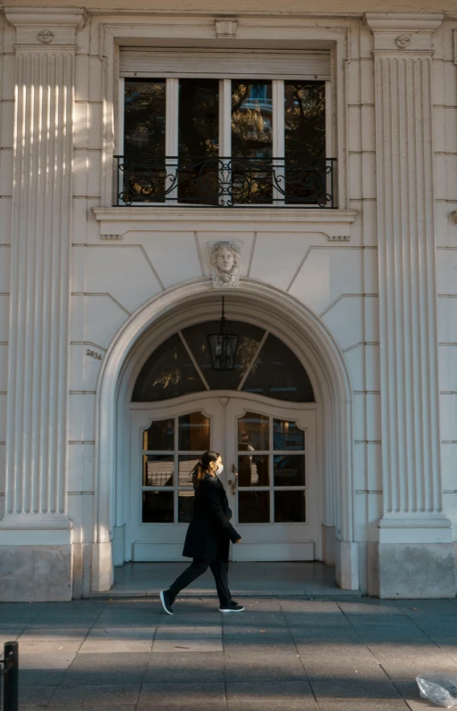 a woman walking past a building entrance with a clock above it