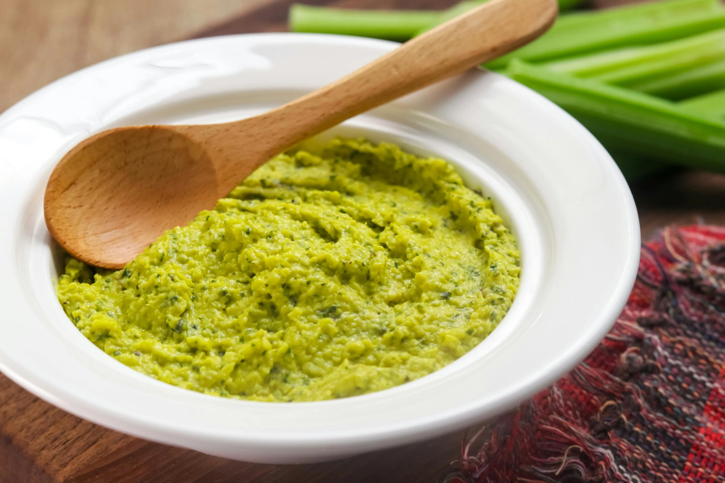 a white bowl with green hummus and a wooden spoon